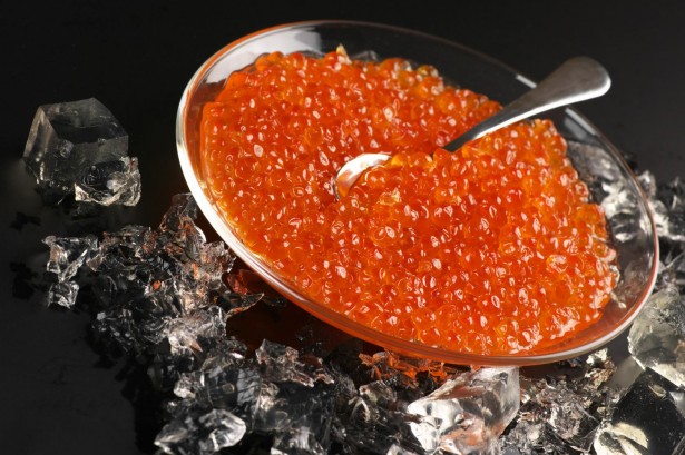 9402511 - salmon caviar in glass plate with spoon and ice on black background.
