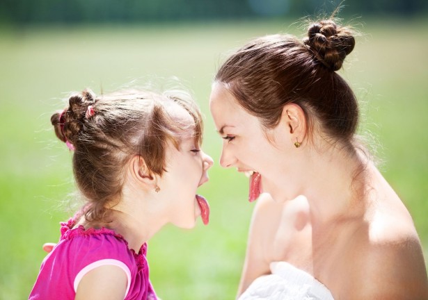beautiful young mother and her daughter in the park on a sunny summer day having fun and showing tongue (focus on the woman)